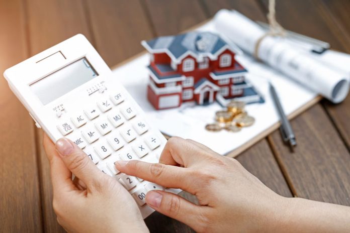 a-female-hand-operating-a-calculator-in-front-of-a-villa-house-model